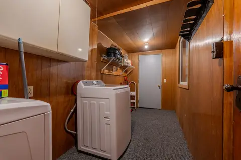 Wood-paneled laundry room with a top-load washer, a dryer, and wall shelves