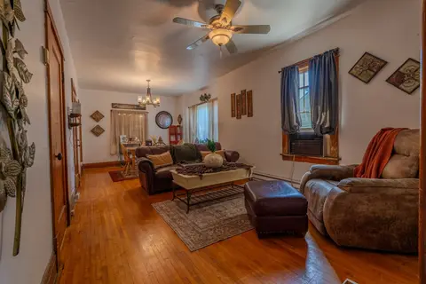Living room with a leather sofa, a recliner, an ottoman, and a ceiling fan over wood floors