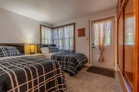 Bedroom with two twin beds in plaid bedding, a bedside lamp, and a glass-paneled door with a curtain
