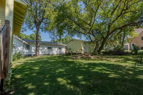 Backyard lawn under mature trees, with a small outbuilding at the back