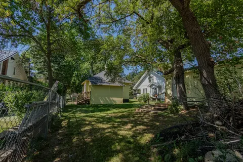 Fenced backyard under tall trees, looking back toward the yellow house