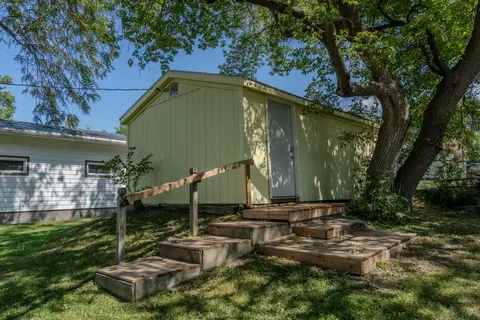 Outbuilding with wood steps and a handrail under a large tree