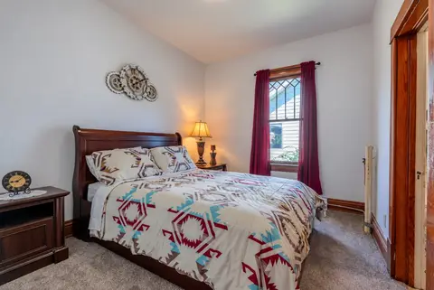 Queen bedroom with a sleigh bed, patterned bedding, a bedside lamp, and a red-curtained window