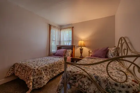 Bedroom with two twin beds in floral bedding, one with a white iron frame, and a corner window