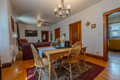 Dining table for four under a chandelier, with the living room and wall-mounted TV behind