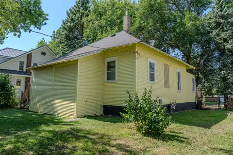 Back of the yellow house with white-trimmed windows and a shrub in the lawn