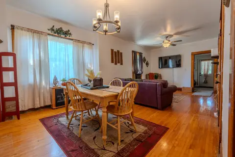 Dining table with four wood chairs, an electric fireplace, and the living room with a wall-mounted TV beyond