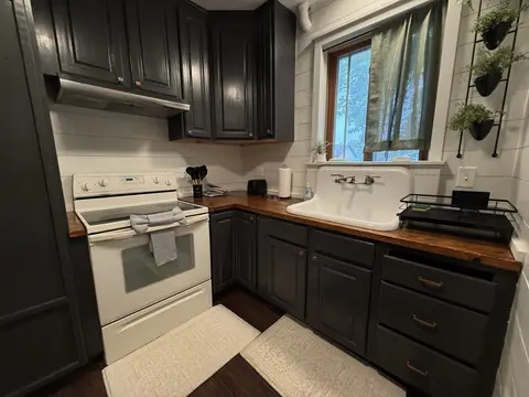 Kitchen corner with a white range, dark cabinets, and a farmhouse sink under a window