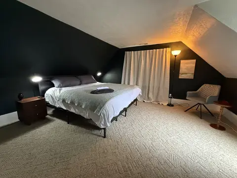 King bedroom with a sloped ceiling, white curtains, and a reading chair