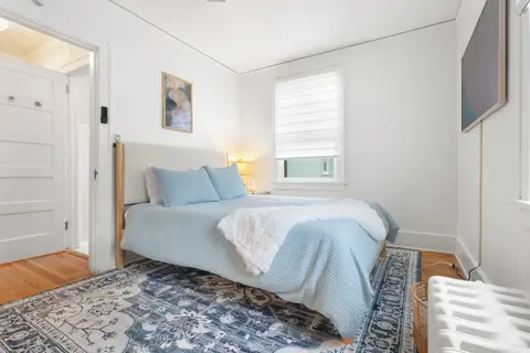 Bedroom with a queen bed in soft blue, a patterned rug, and an original radiator