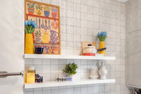 Kitchen open shelves with a folk-art print, tulips in yellow vases, and a blue Dala horse