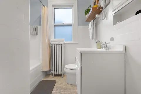 Bathroom with a tub and shower, a penny tile floor, an original radiator, and wall-mounted dispensers