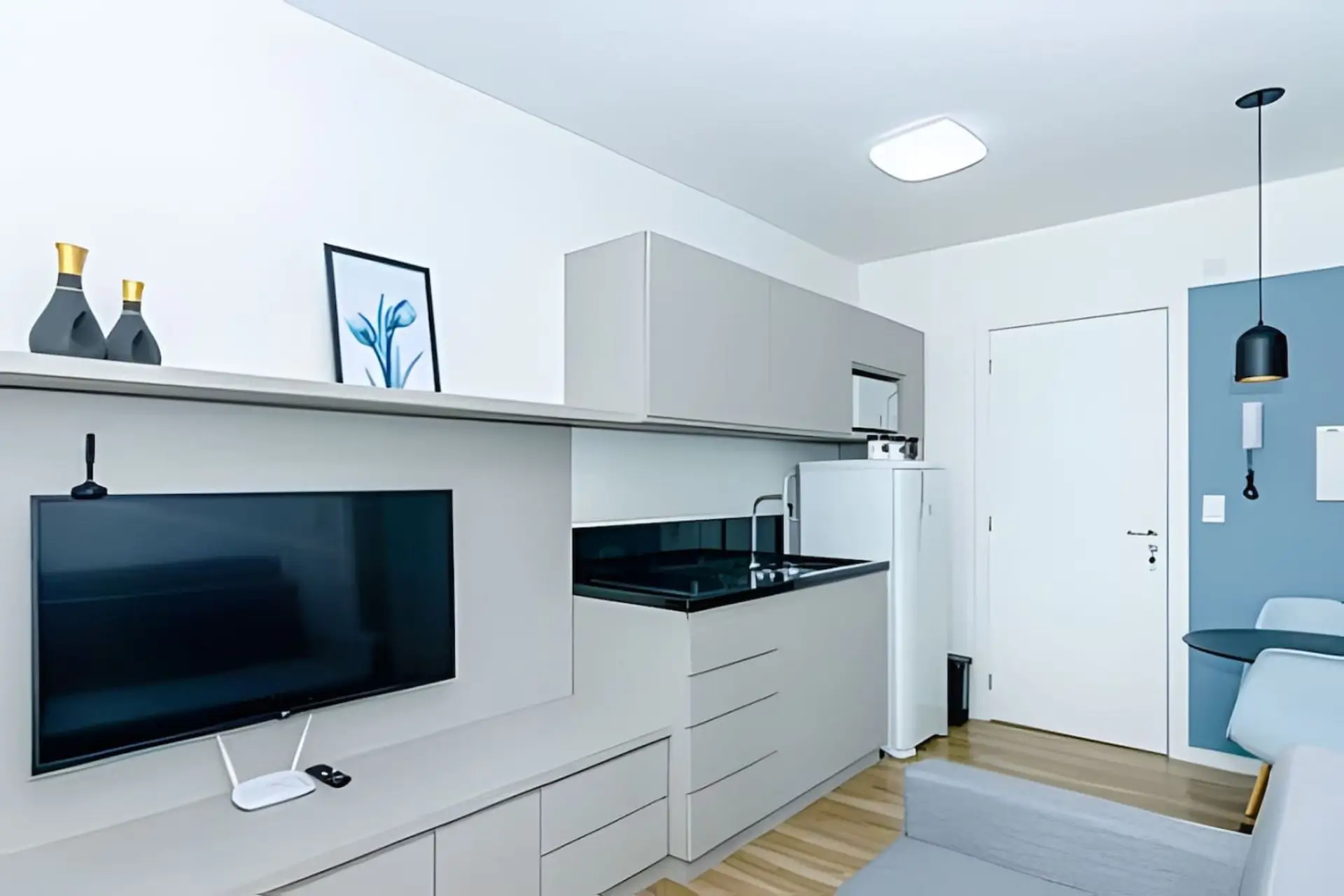 Sala/Cozinha com televisão, cooktop de indução, pia, geladeira e armários.