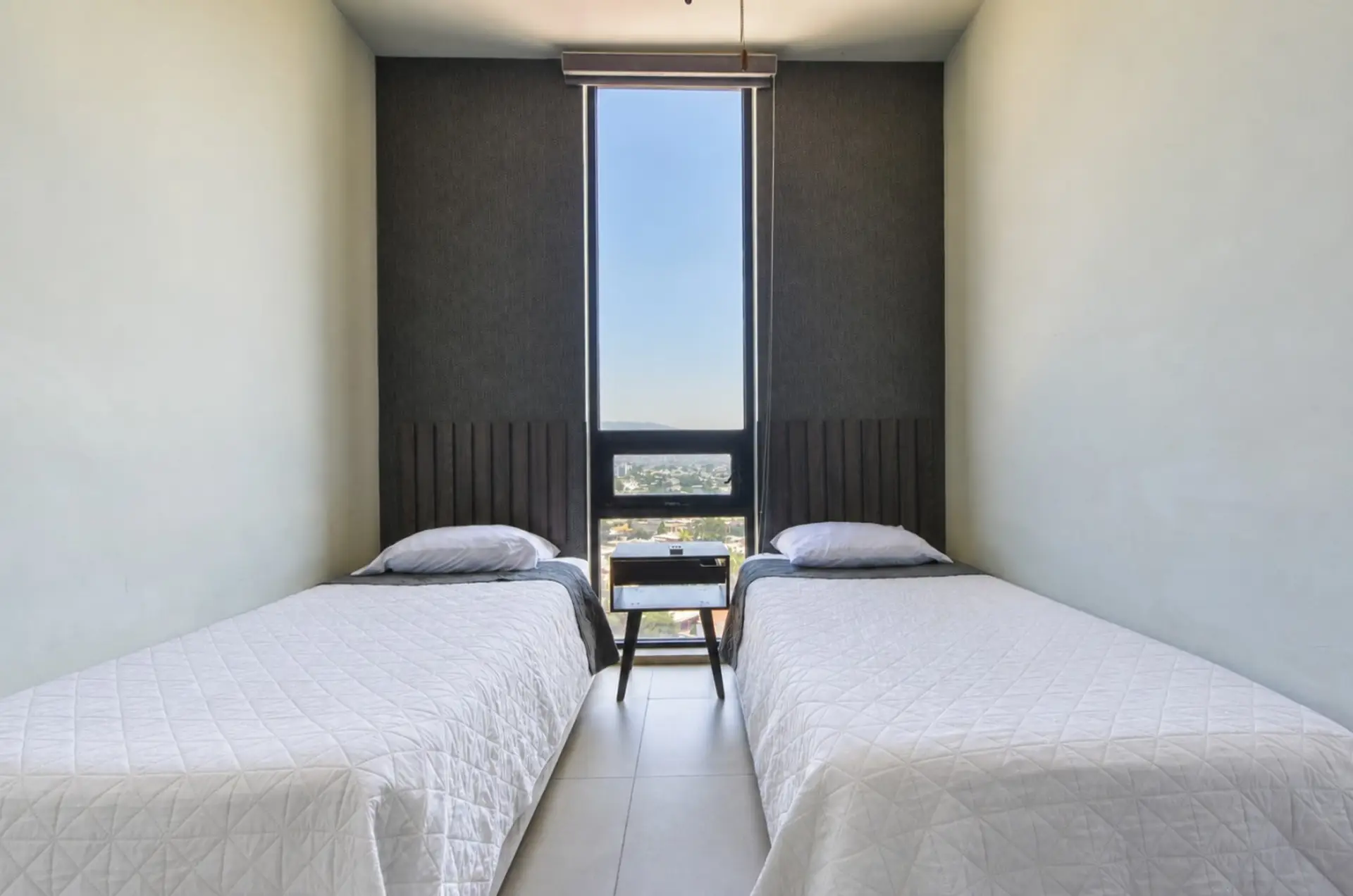 Habitación B con 2 camas individuales, clóset, abanico y cortinas. Incluye colchas y almohadas para un descanso cómodo y tranquilo.
