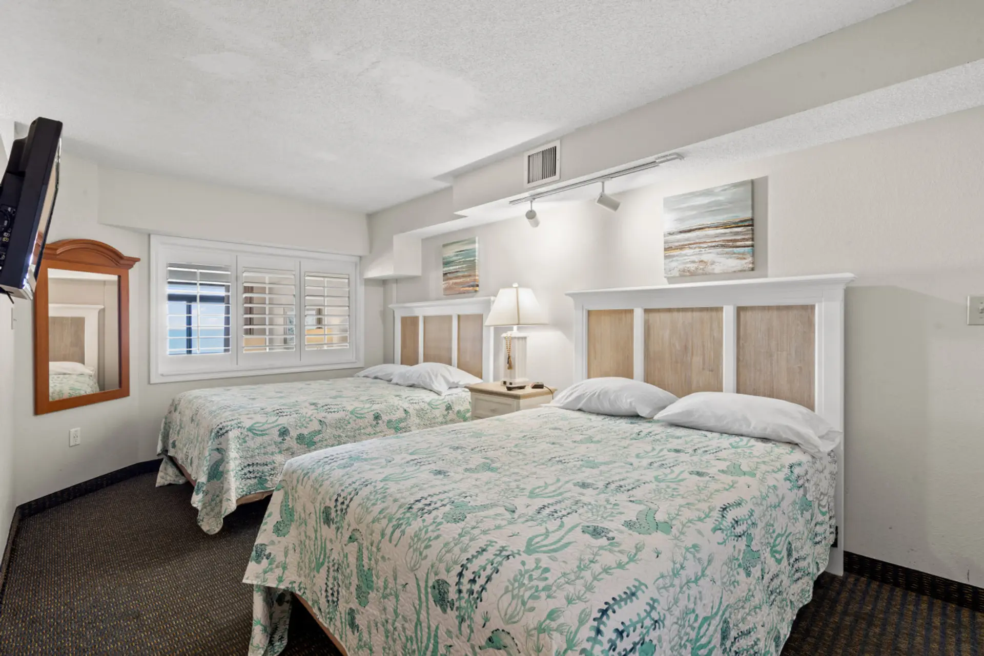 Master bedroom with two plush queen beds, a smart TV, and a chest of drawers for extra storage.