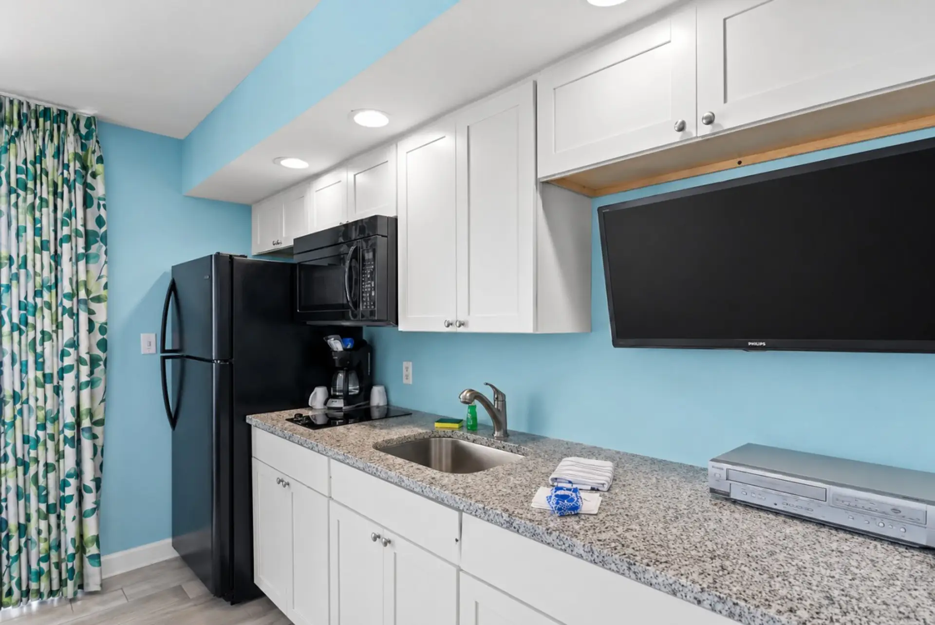 A cheerful coastal-blue kitchen stocked with everything you need — full-size fridge, microwave, two-burner cooktop, and coffee maker for lazy mornings before the beach.