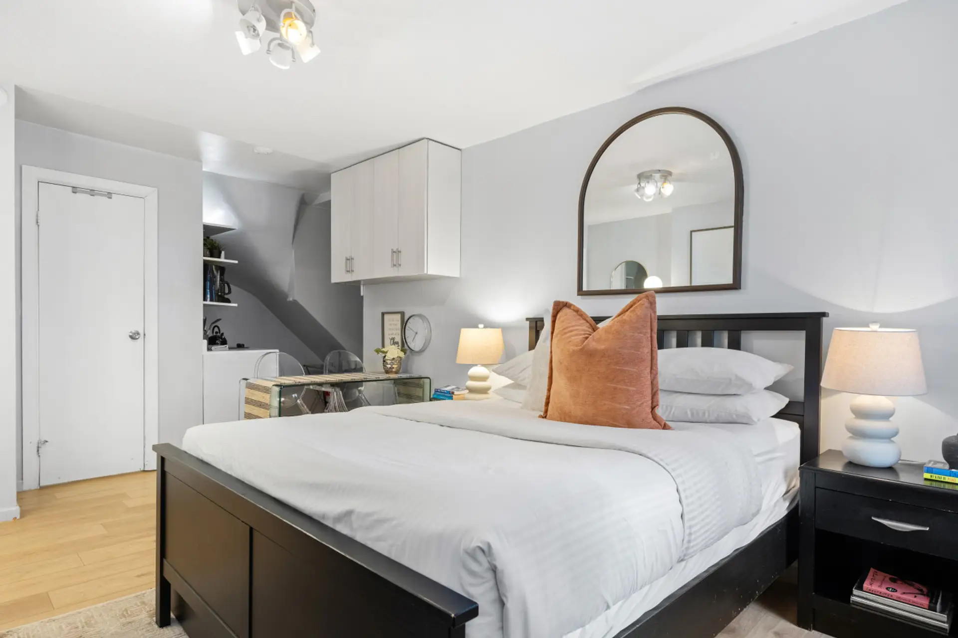 A sleek dining/workspace sits beside a compact kitchenette with ample storage. Warm lighting and modern finishes create a stylish, functional space.