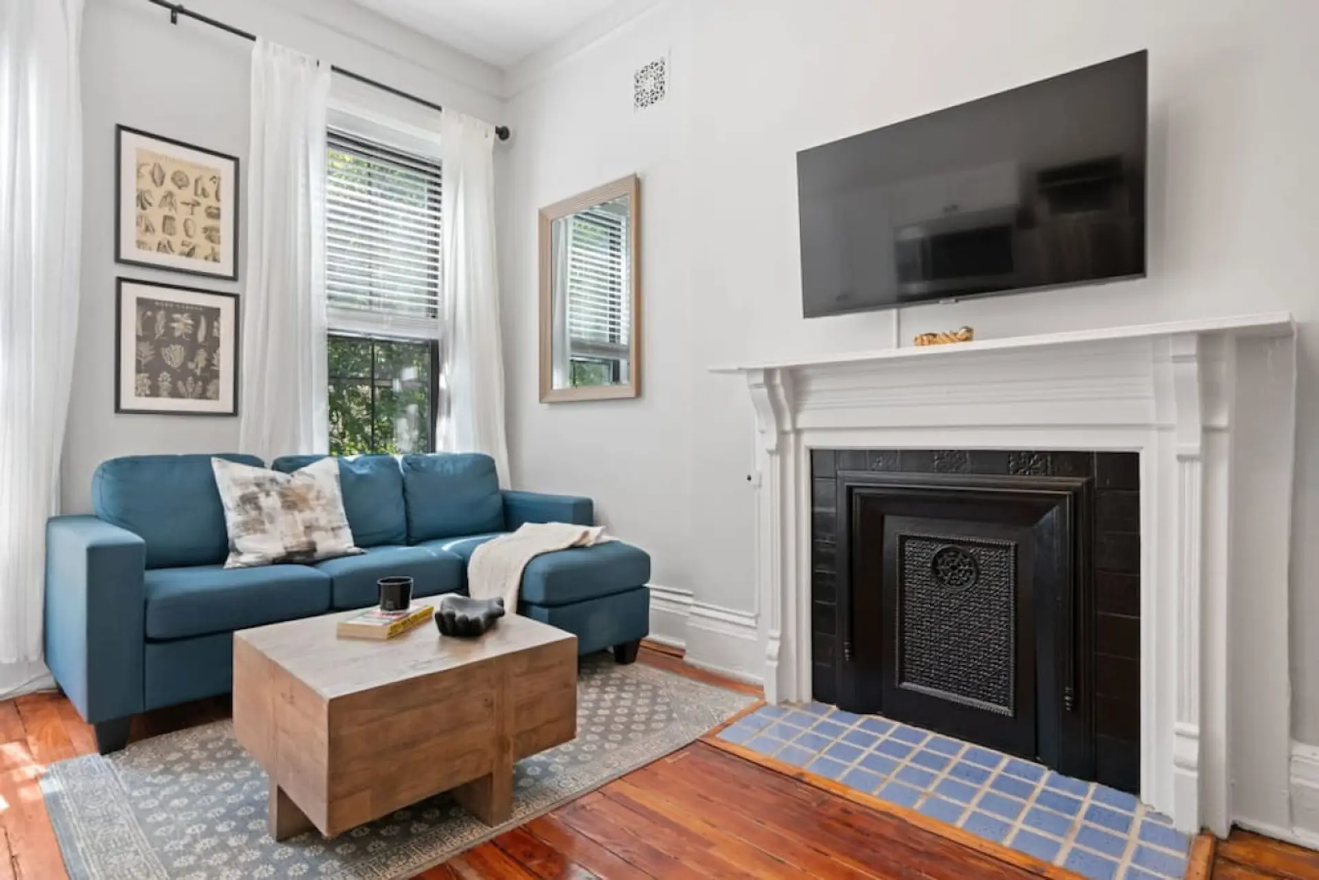 The living room features a roomy layout, complete with a large smart TV for entertainment. Sunlight streams through the wide window, creating a bright, inviting atmosphere.