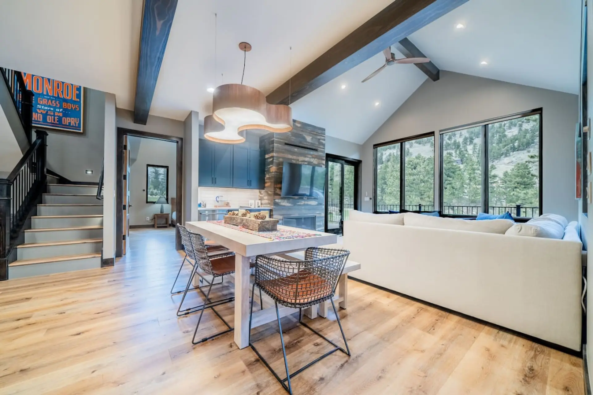 Open-concept living, dining, and kitchen with soaring ceilings and walls of windows overlooking the pines.