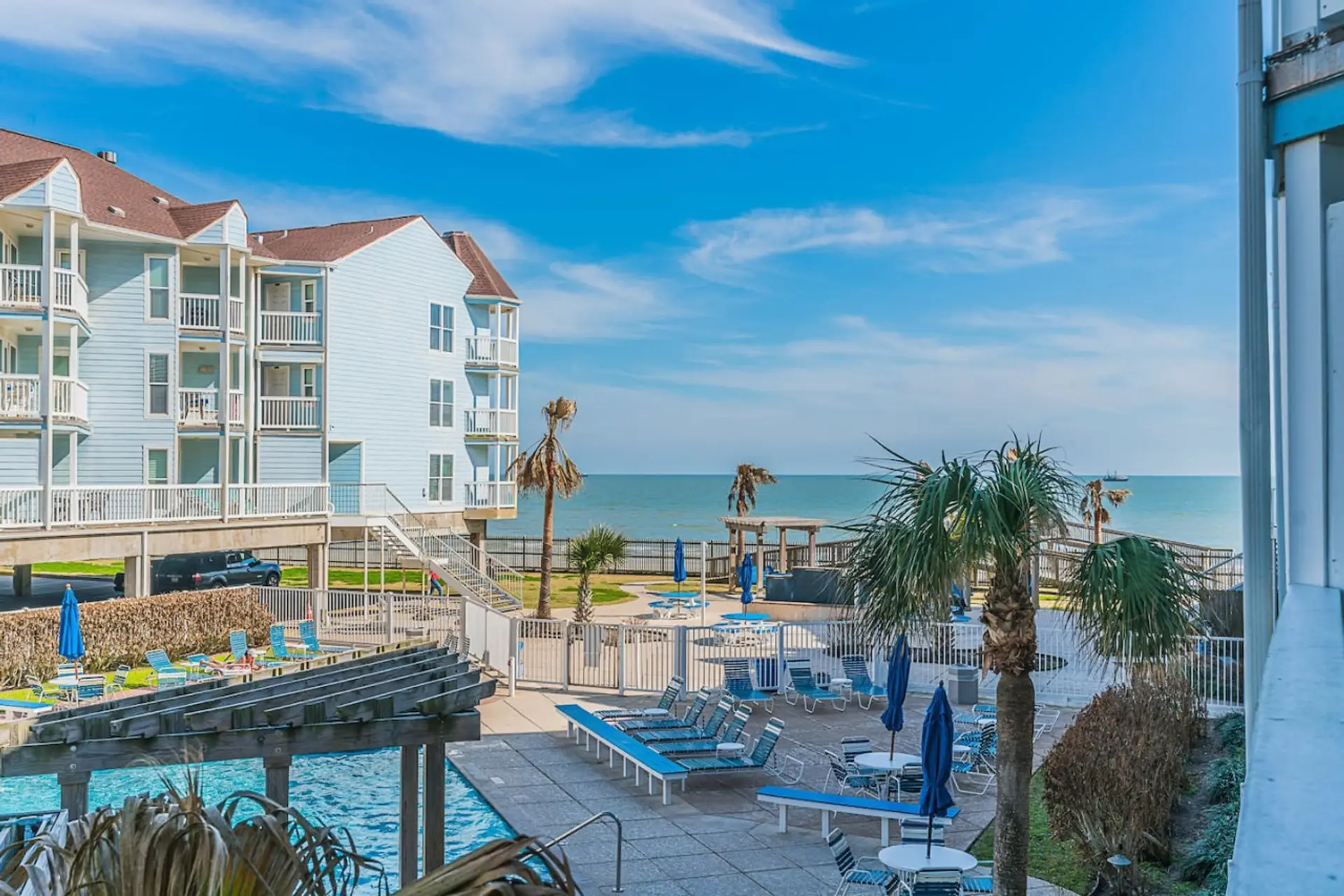 A luxurious resort with a sparkling pool overlooking the ocean, surrounded by lush greenery and palm trees, set against a backdrop of Gulf of Mexico.