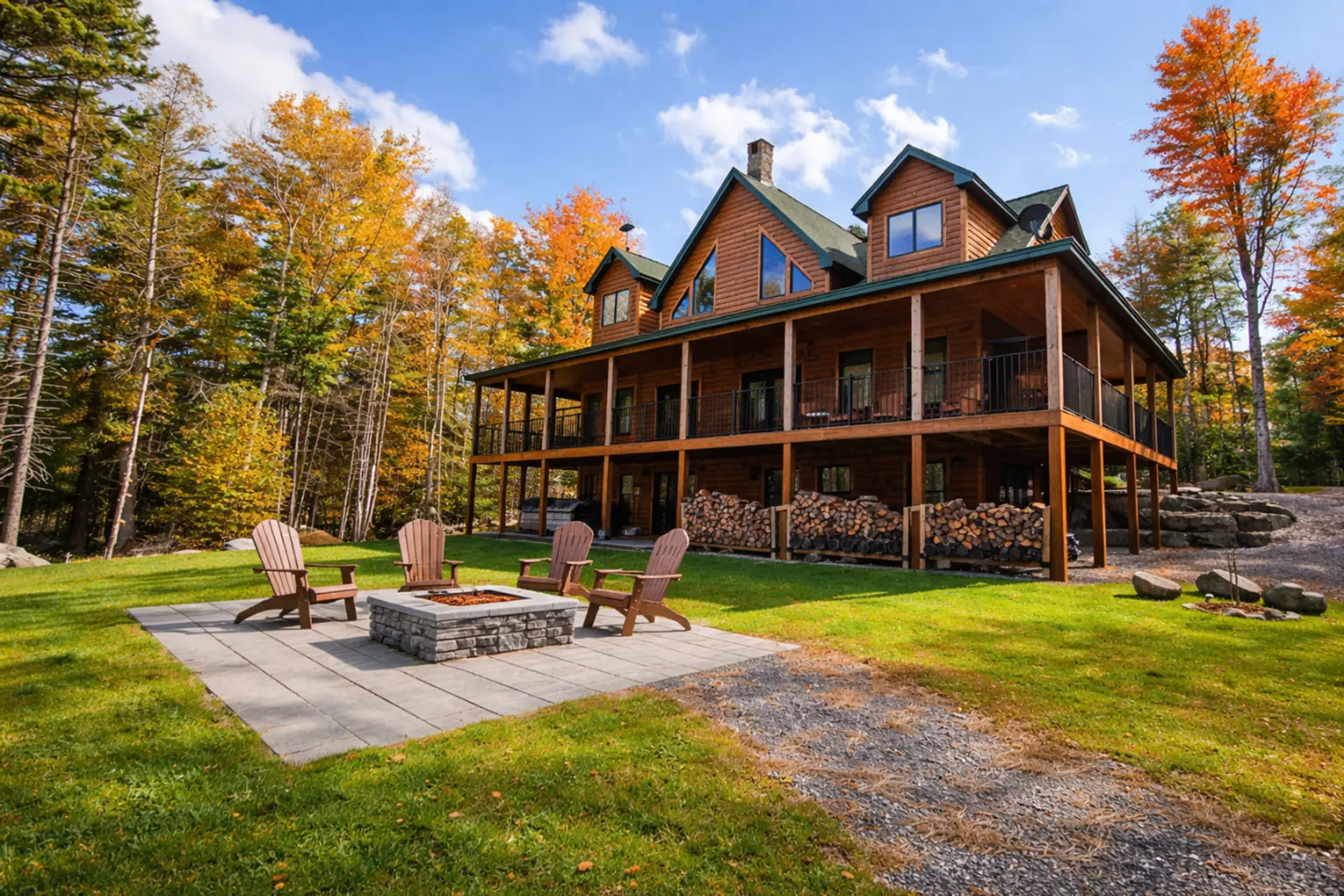 Large log cabin with a wraparound porch, outdoor fire pit, and spacious yard surrounded by beautiful trees and seasonal views.
