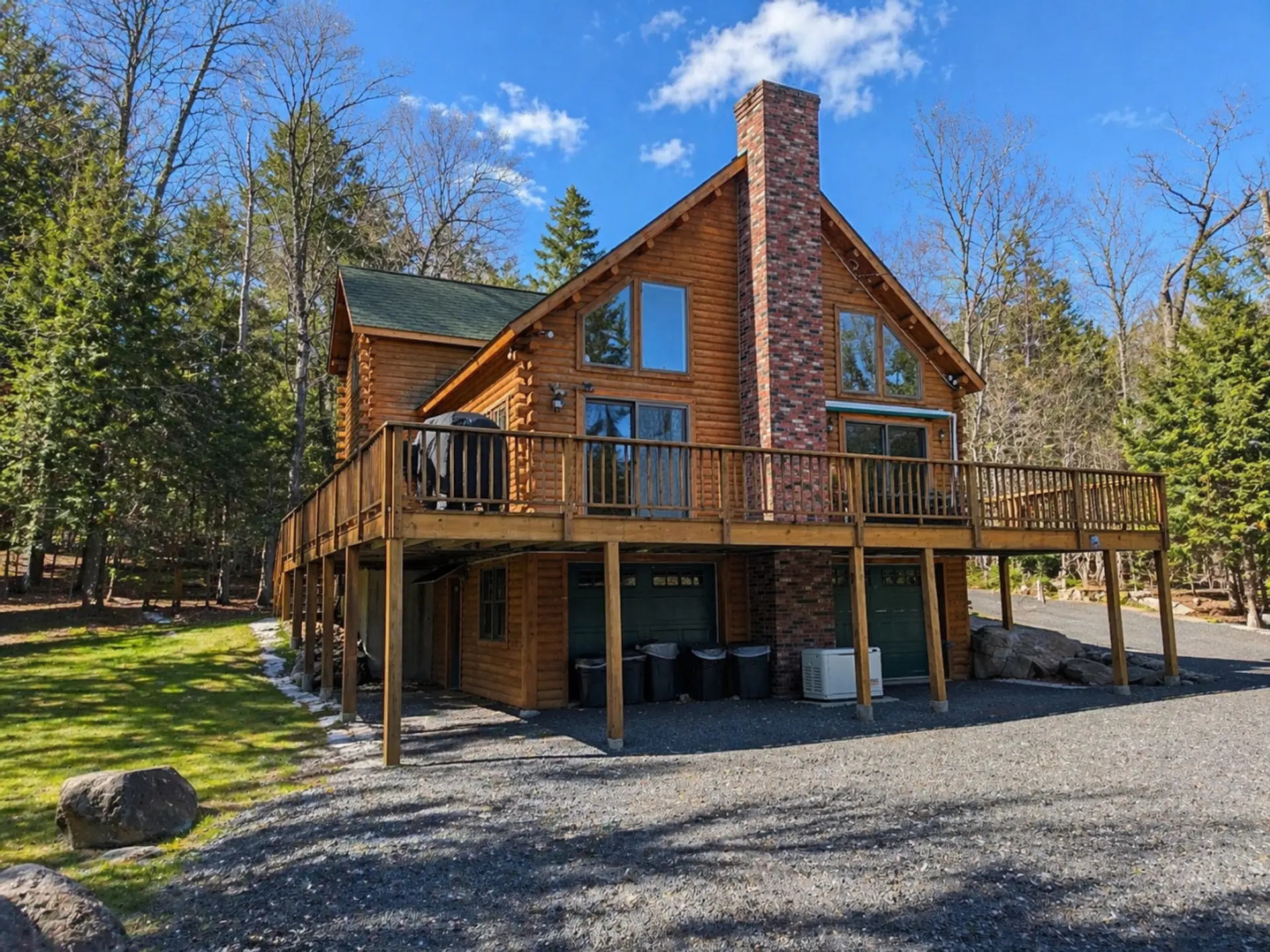 Spacious log cabin with a wraparound deck, towering fireplace, and peaceful wooded surroundings.