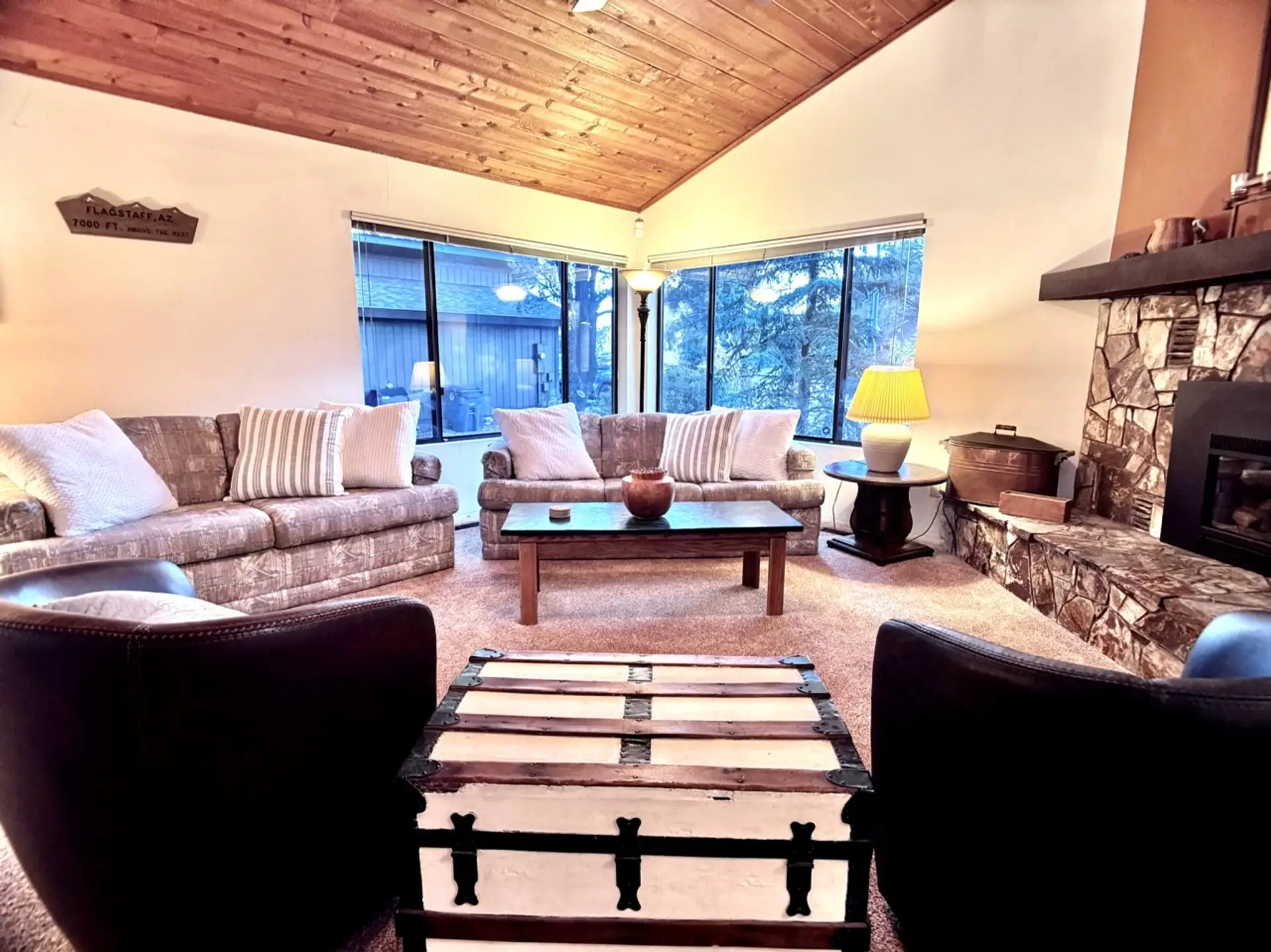 Spacious living room with vaulted wood ceilings, large windows, and a gas fireplace.