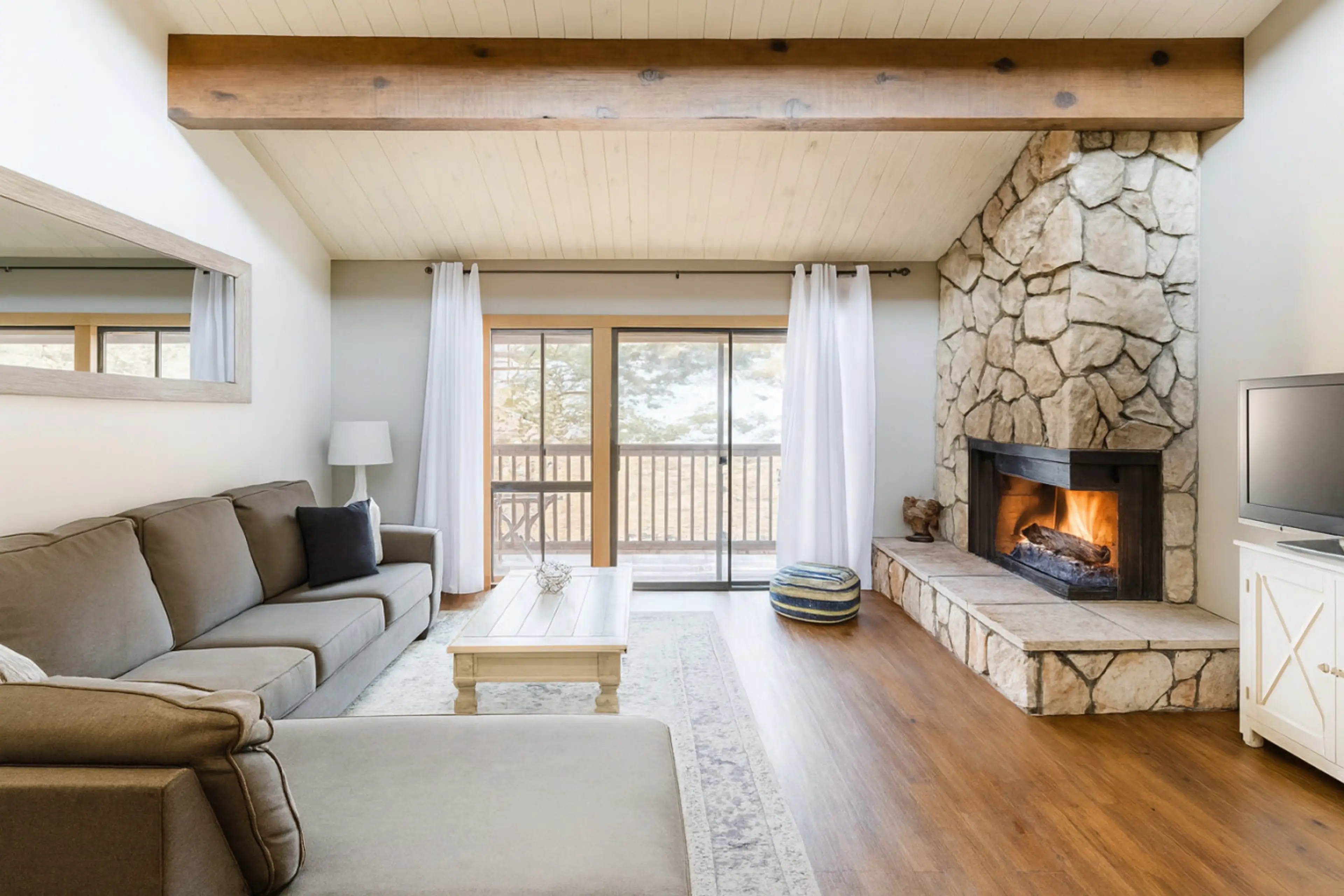 Cozy living room featuring a large, comfortable sofa, high ceilings, and a beautiful stone fireplace—perfect for relaxing after a day on the mountain. Step out onto the private balcony and enjoy incredible views where you can actually watch skiers coming 