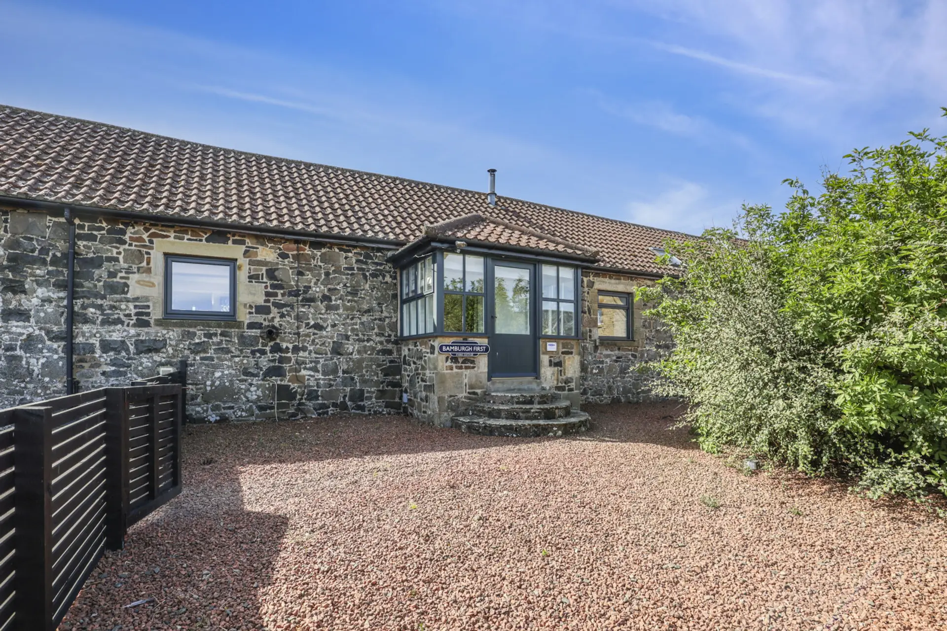 Exterior of sandstone stable cottage with gravel courtyard and bay window.