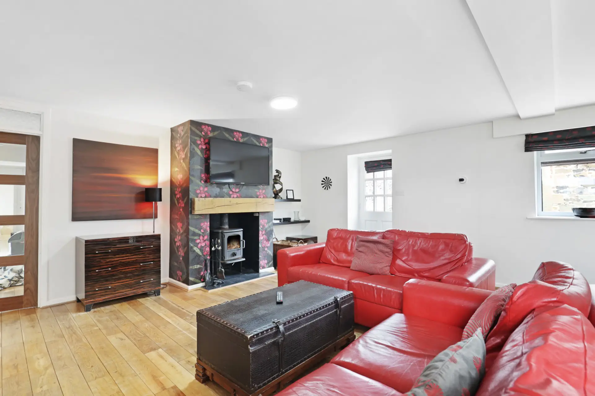 Open-plan lounge with red leather sofas and wood-burning stove.