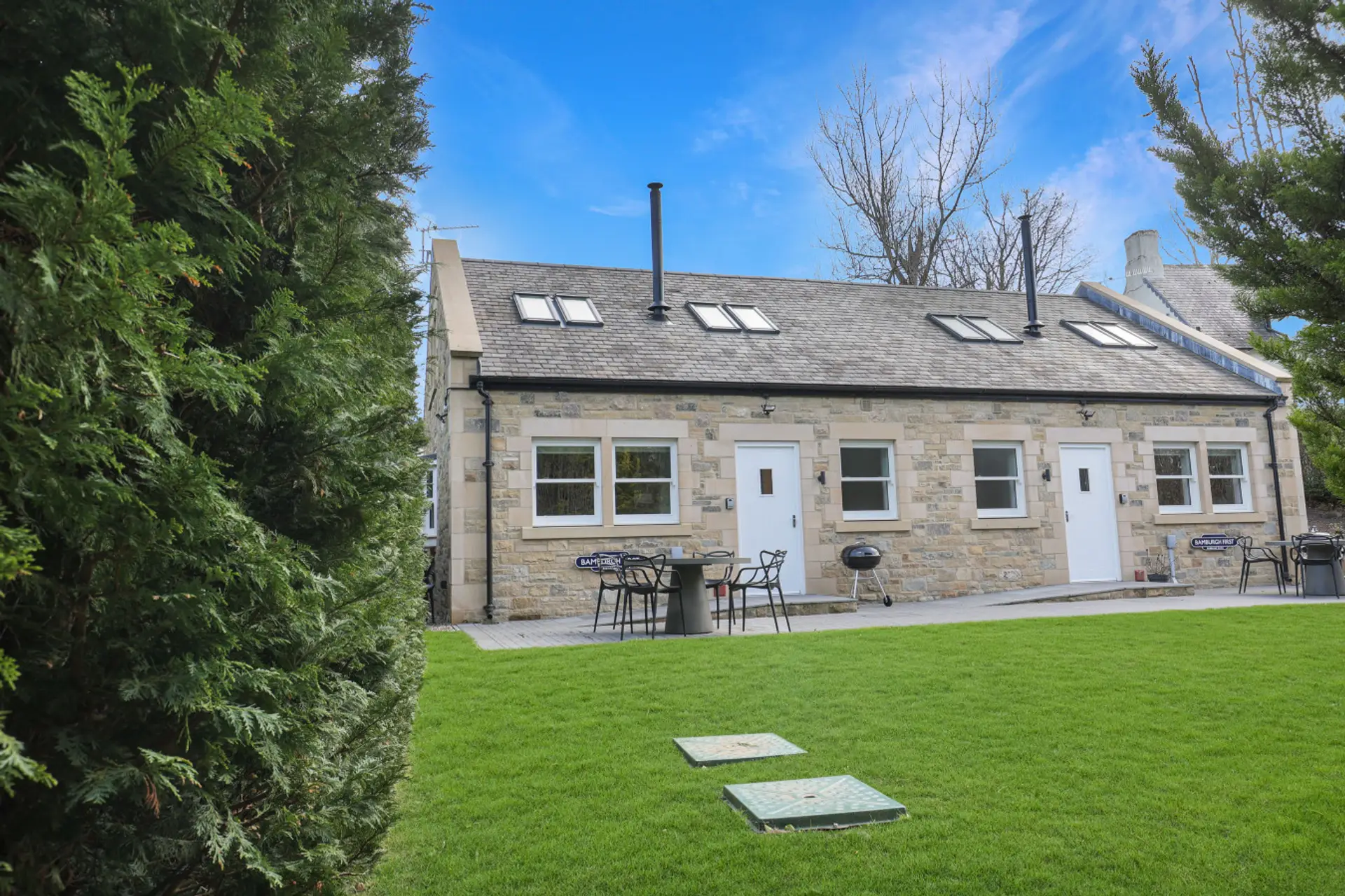 Stone-built exterior of Birdsong Cottage with shared lawn and patio seating