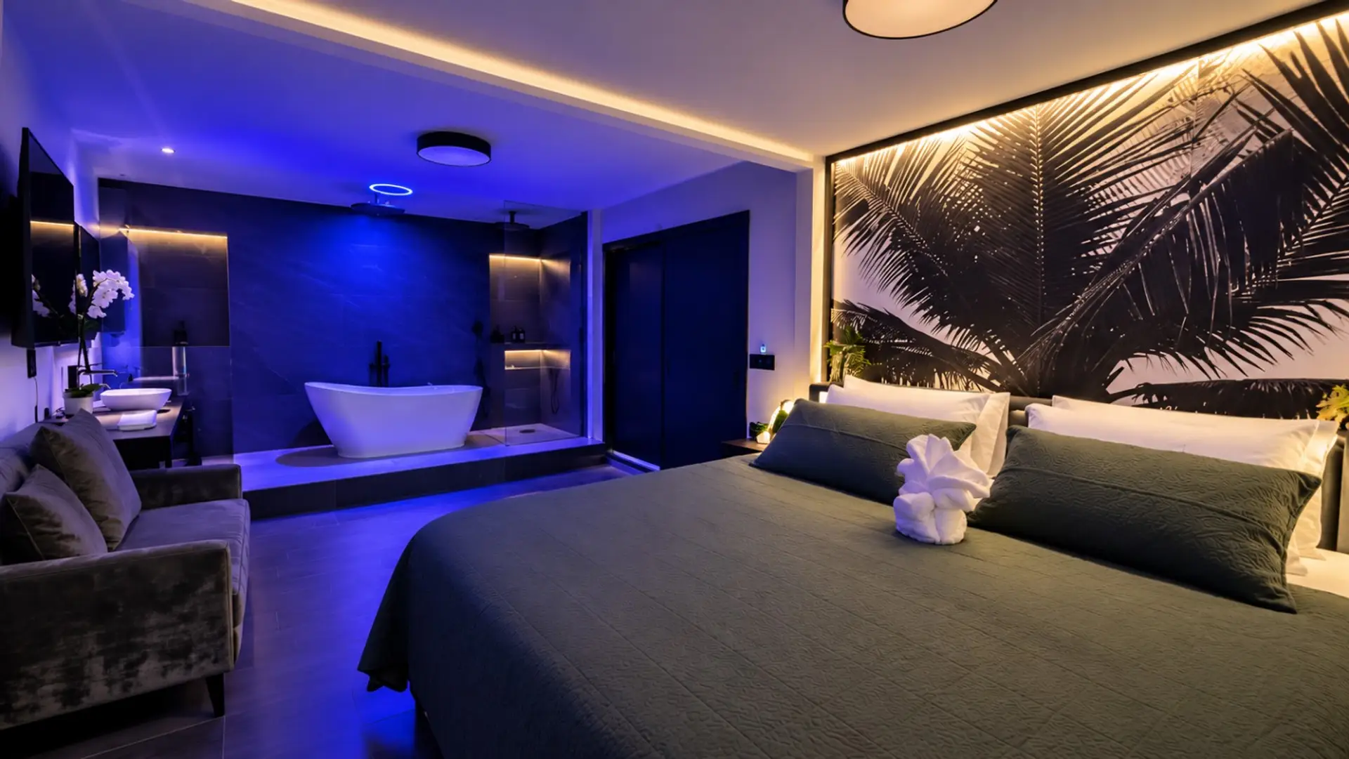 Elegant master bedroom with a luxurious open-concept spa bathroom, freestanding soaking tub, rainfall shower, ambient blue lighting, and tropical-inspired décor. A private, romantic retreat designed for ultimate comfort and relaxation.