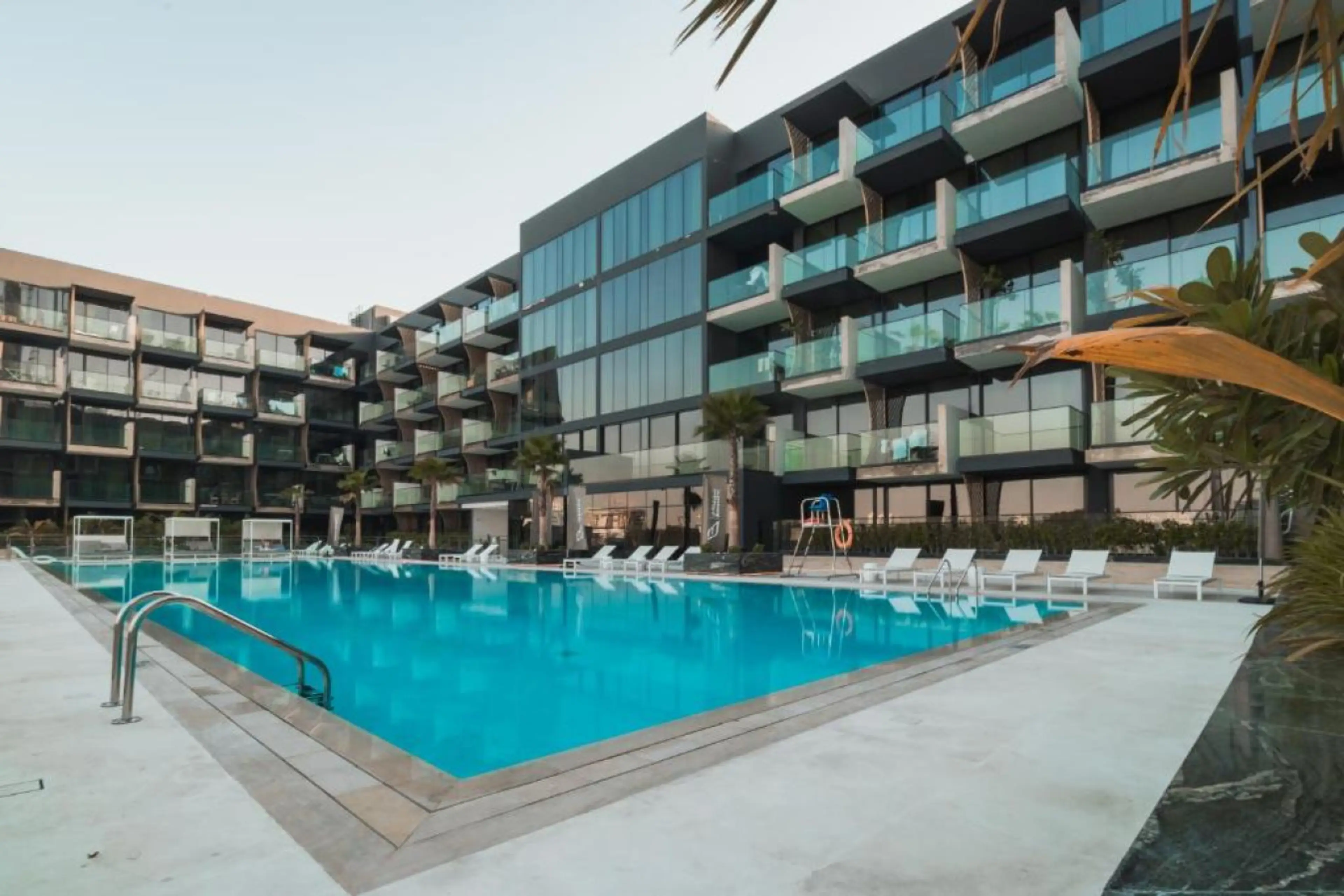 Luxurious apartment complex with a pristine pool, modern design, and private balconies.
